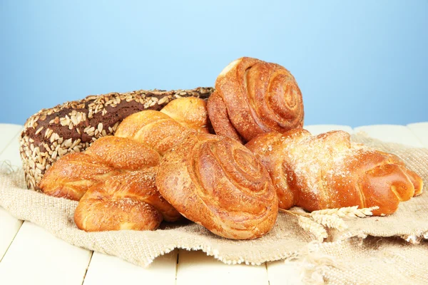 Composition with bread, rolls on sackcloth, on wooden table, on color background — Stock Photo, Image