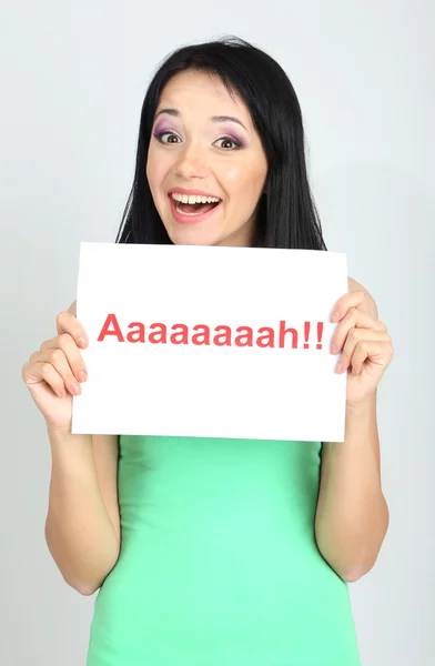 Verrast jonge vrouw houdt inscriptie "ah" op grijze achtergrond — Stockfoto
