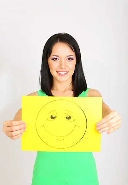 Mujer joven sosteniendo papel con sonrisa feliz sobre fondo gris . —  Fotos de Stock