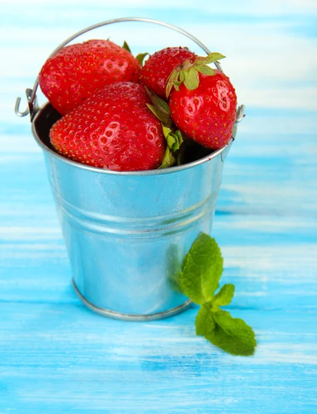 Ripe sweet strawberries in metal pail on blue wooden table — Stock Photo, Image