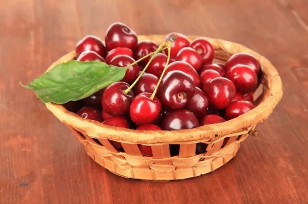 Cherry bessen in rieten mand op houten tafel close-up — Stockfoto