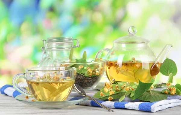 Kettle and cup of tea with linden on wooden table on nature background — Stock Photo, Image