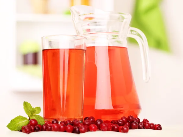 Werper en glas cranberry sap met rode veenbessen op tafel — Stockfoto