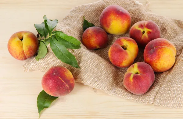 Peaches on sackcloth on wooden table — Stock Photo, Image