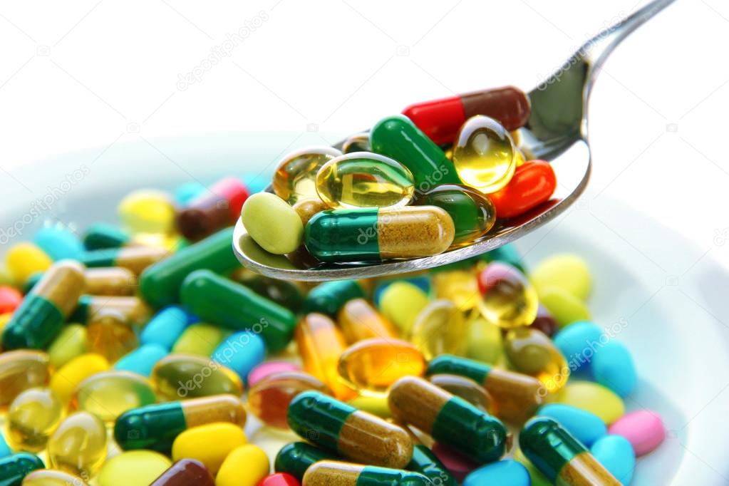 Colorful capsules and pills on plate with spoon, close up