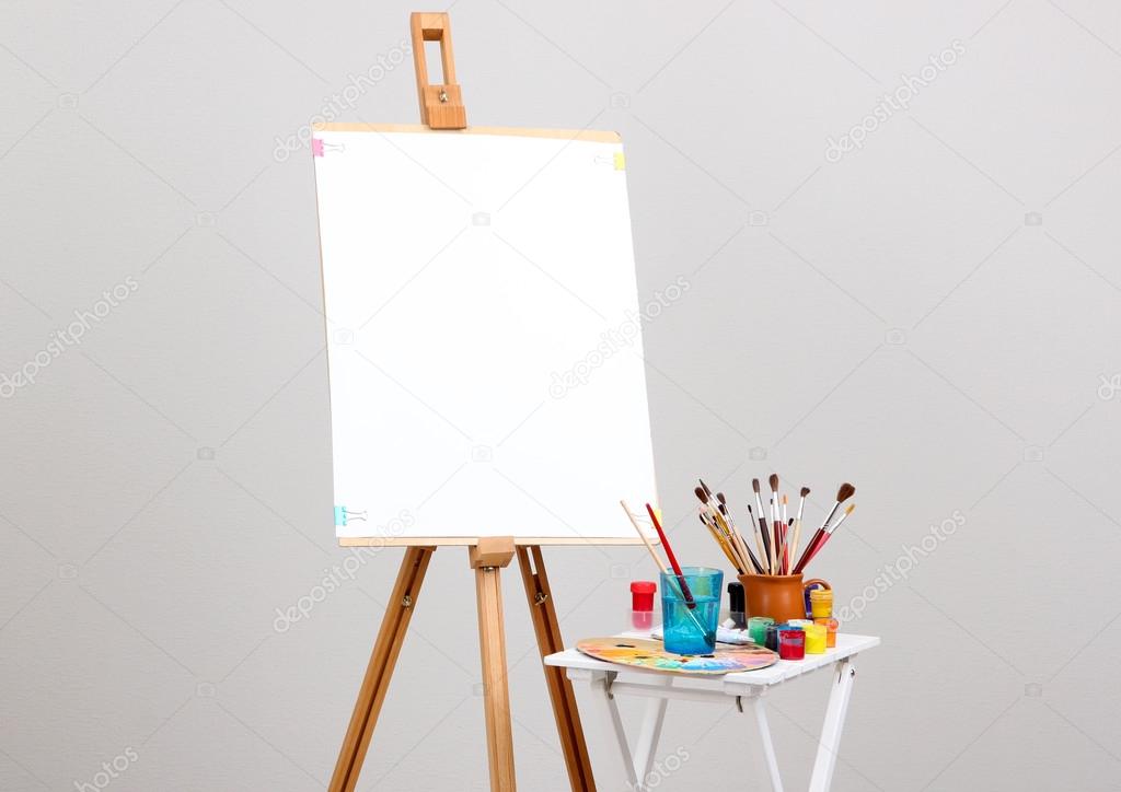 Wooden easel with clean paper and art supplies in room Stock Photo by  ©belchonock 27894753