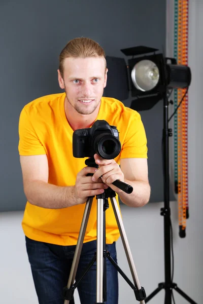 Fotógrafo bonito com câmera no trabalho, no fundo do estúdio de fotografia — Fotografia de Stock