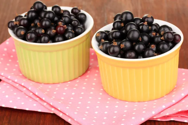 Fresh black currant in bowls on napkin on wooden background — Stock Photo, Image