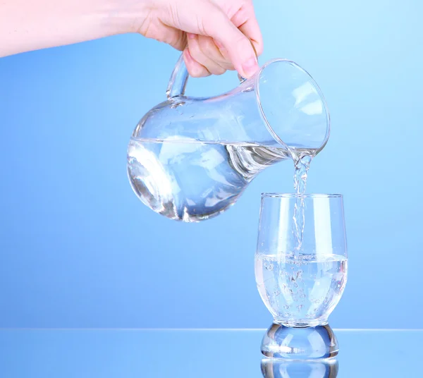 Glass pitcher of water and glass on blue background — Stock Photo, Image