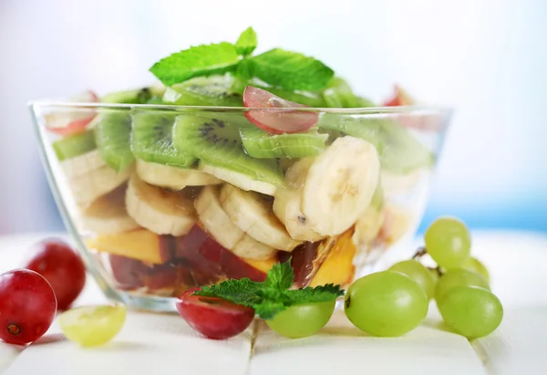 Salade de fruits savoureuse dans un bol en verre, sur une table en bois blanc — Photo