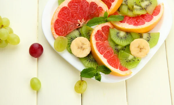 Surtido de frutas en rodajas en plato, sobre mesa de madera blanca — Foto de Stock