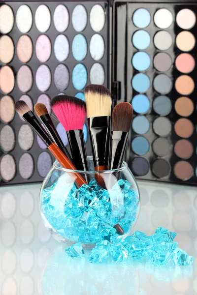 Make-up brushes in a bowl with stones on palette of shadows background — Stock Photo, Image