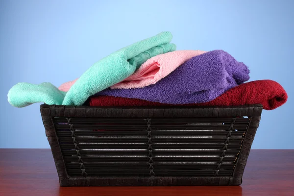 Bunte Handtücher im Korb auf farbigem Hintergrund — Stockfoto