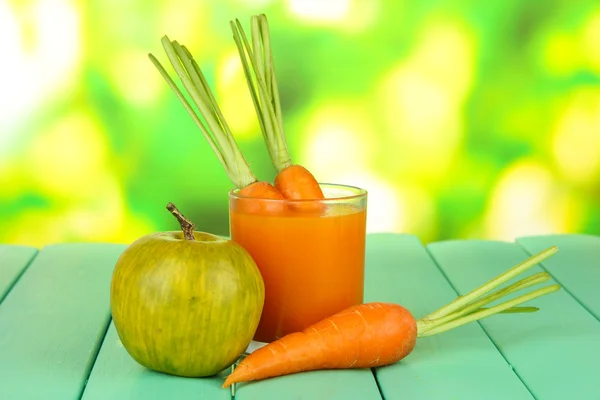 Heap of carrots and green apple, glass of juice, on color wooden table on bright background — Stock Photo, Image