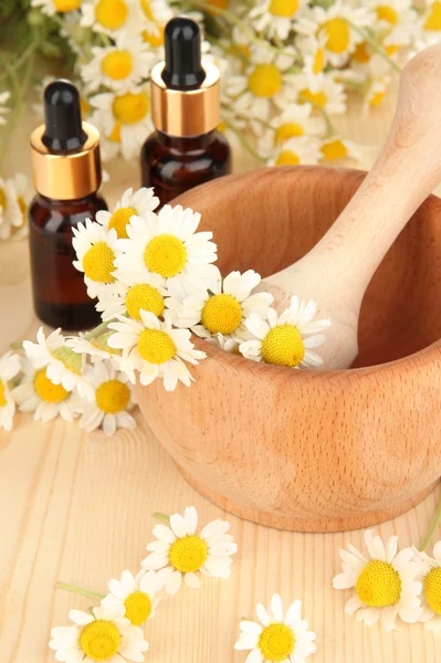 Aceite esencial y flores de manzanilla en mortero sobre mesa de madera — Foto de Stock