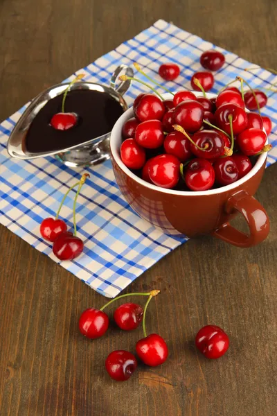 Bagas de cereja vermelhas maduras em xícara e molho de chocolate em mesa de madeira close-up — Fotografia de Stock