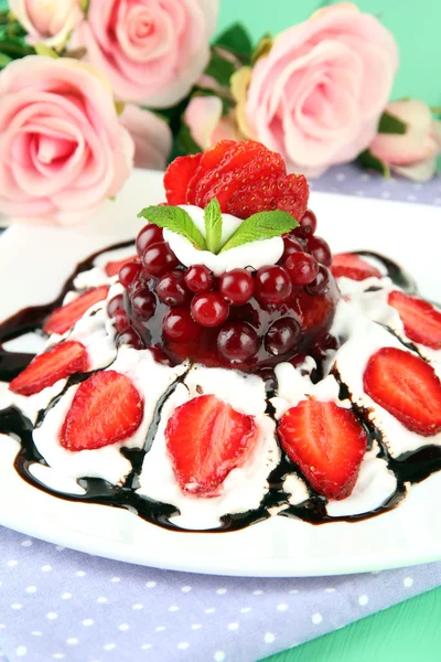 Вкусный желейный десерт со свежими ягодами, на фоне розовых роз — стоковое фото
