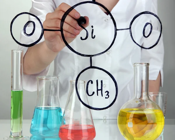 Хімічна жінка пише формули на склі на сірому фоні — стокове фото