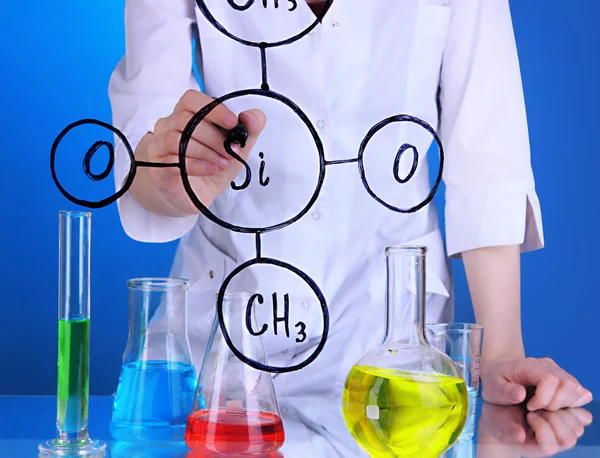 Chemist woman writing formulas on glass on blue background — Stock Photo, Image