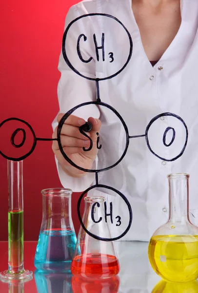 Chemik kobieta zapisywania wzorów na szkle, na czerwonym tle — Zdjęcie stockowe