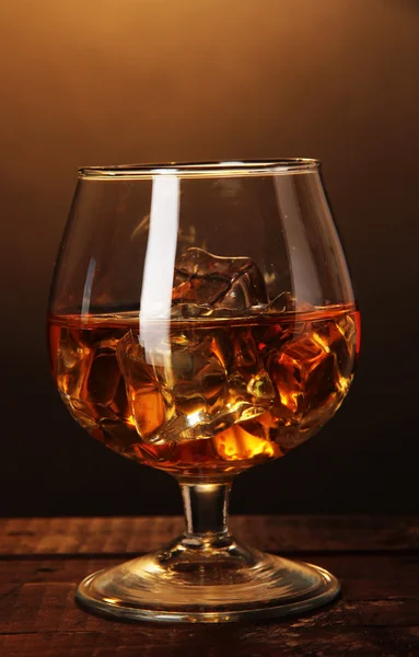 Brandy glas met ijs op houten tafel op bruine achtergrond — Stockfoto