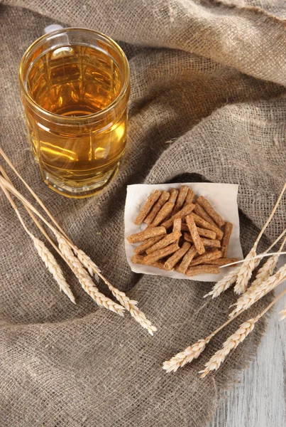 Beer in glass and crackers on bagging on wooden table — Stock Photo, Image