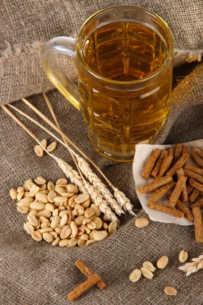 Bier in het glas, crackers en noten op zakken op houten tafel — Stockfoto
