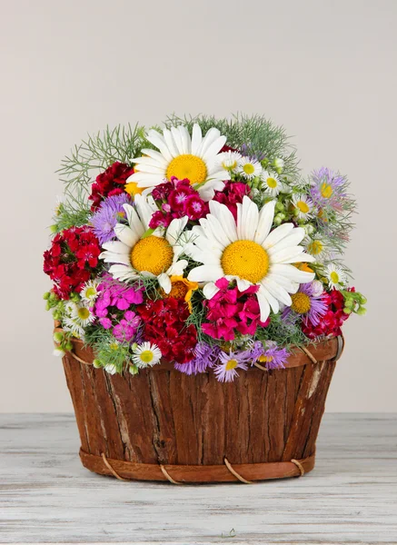 Krásné světlé květy v dřevěné koše na stole na šedém pozadí — Stock fotografie