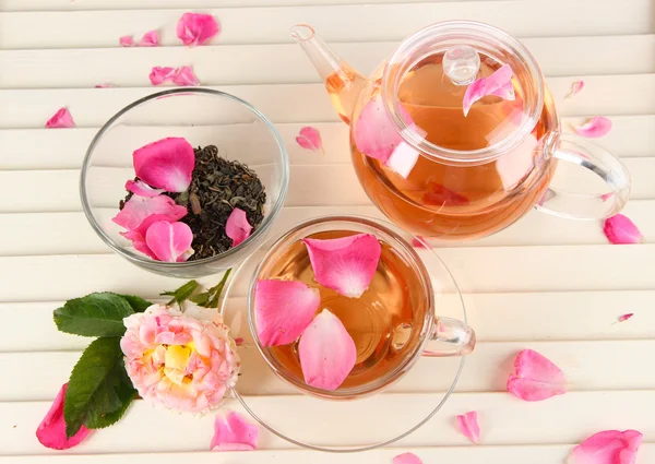 Konvice a šálek čaje z tea rose na dřevěné pozadí — Stock fotografie