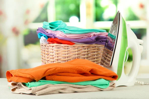 Steam iron and wicker basket with clothes, on bright background — Stock Photo, Image