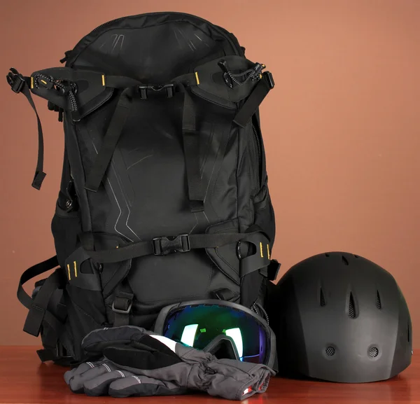 Wintersportbrille, Helm und Handschuhe, Rucksack, auf braunem Hintergrund — Stockfoto