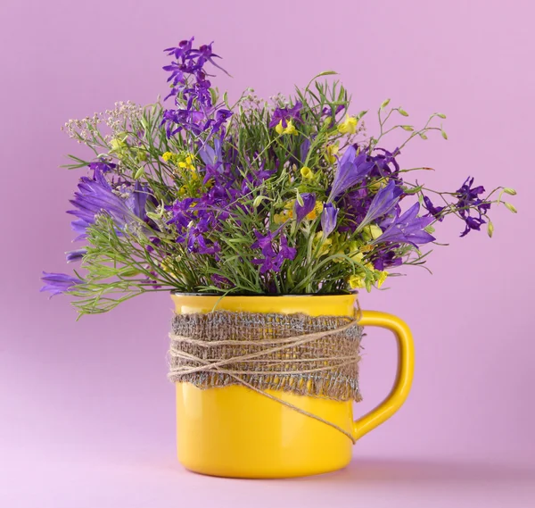 Schöner Strauß Wildblumen in Tasse auf violettem Hintergrund — Stockfoto