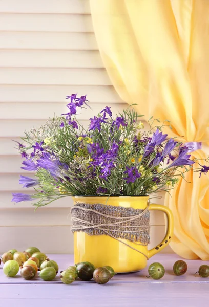 Gyönyörű csokor vadvirágok kupa és a bogyók a fából készült asztal — Stock Fotó