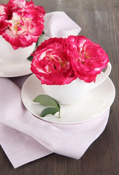Roses in cups on napkin on wooden background — Stock Photo, Image