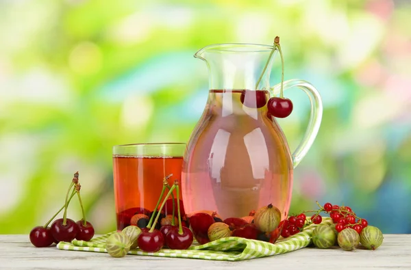 Pitcher and glass of compote with summer berries on natural background — Stock Photo, Image