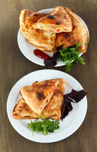 Pizza calzones on plates on wooden table — Stock Photo, Image