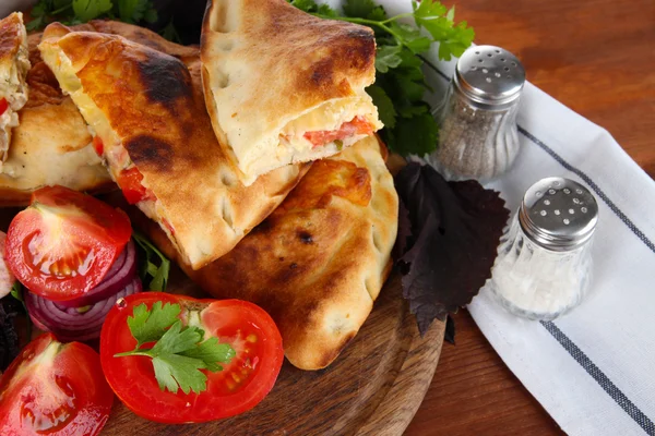 Pizza Calzone na dřevěné desce poblíž ubrousek na dřevěný stůl — Stock fotografie