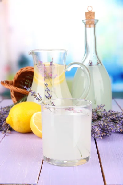 Lavender lemonade in glass bottle and jug, on violet wooden table, on bright background — Stock Photo, Image