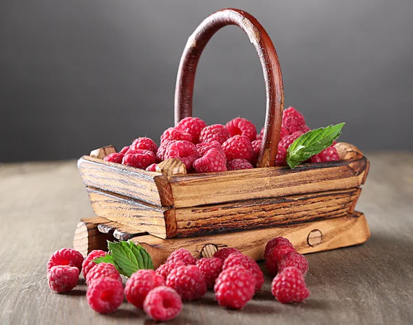 Ripe sweet raspberries in basket on wooden table, on grey background — Stock Photo, Image