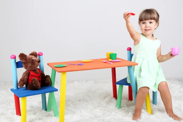 Niña linda sentada en una silla pequeña cerca de la mesa, sobre fondo gris —  Fotos de Stock