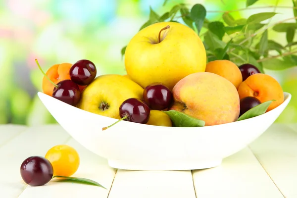 Bright summer fruits in plate on wooden table on natural background — Stock Photo, Image