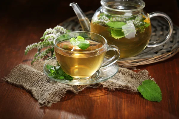 Taza y tetera de té de hierbas con flores de menta fresca en la mesa de madera —  Fotos de Stock