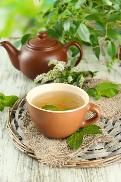 Teekanne und Tasse Kräutertee mit frischen Minzblüten auf Holztisch — Stockfoto