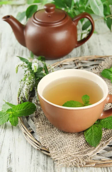 Teiera e tazza di tisana con fiori di menta freschi sul tavolo di legno — Foto Stock