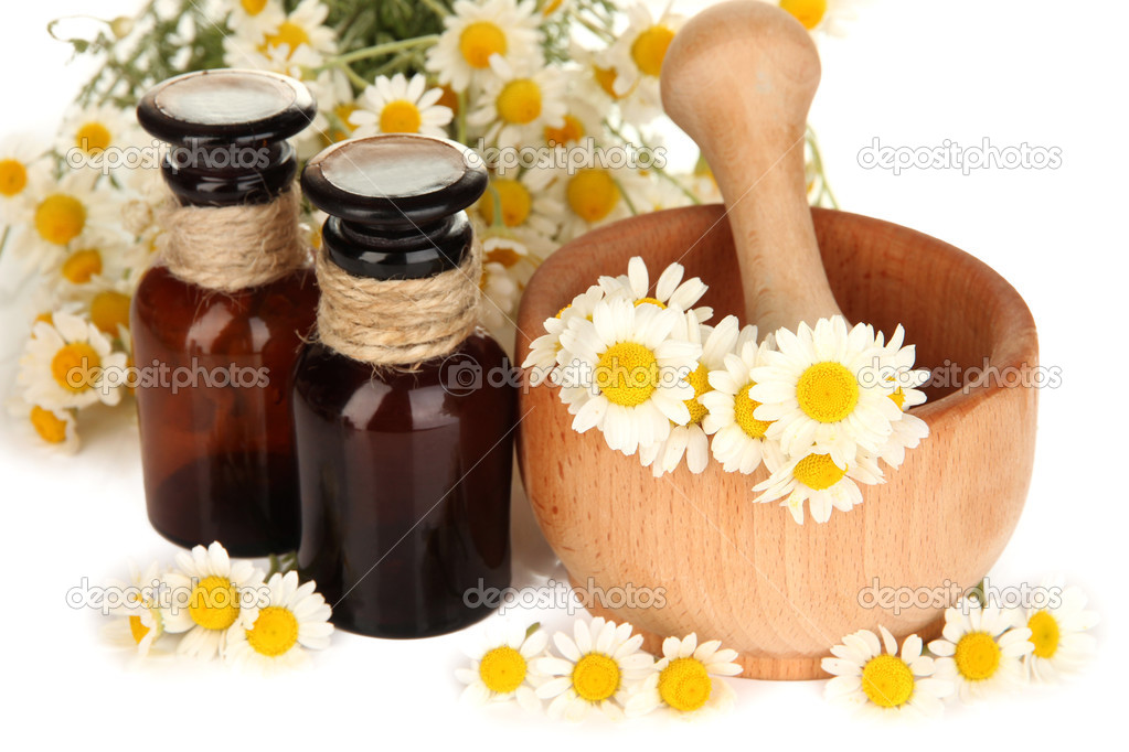 Essential oil and chamomile flowers in mortar close up