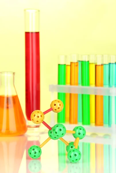 Molecule model and test tubes with colorful liquids on yellow background — Stock Photo, Image