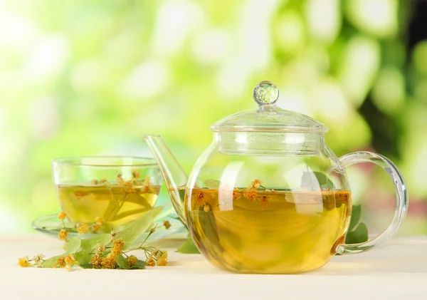 Kettle and cup of tea with linden on wooden table on nature background — Stock Photo, Image