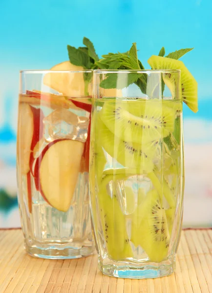 Gläser mit Fruchtgetränken mit Eiswürfeln auf blauem Hintergrund — Stockfoto