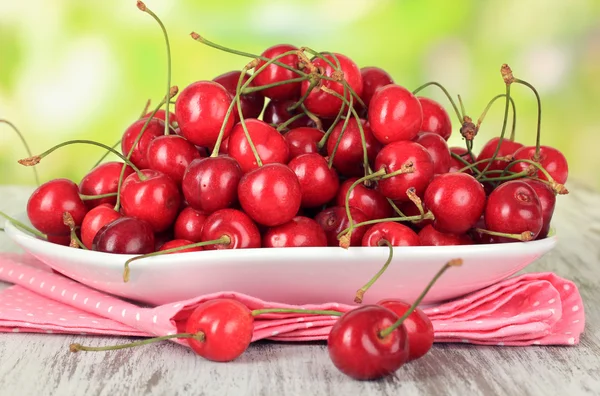 Cherry berries on plate on wooden table on bright background — Stock Photo, Image