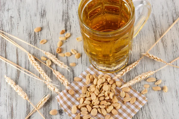 Cerveza en vaso y nueces en servilleta sobre mesa de madera — Foto de Stock